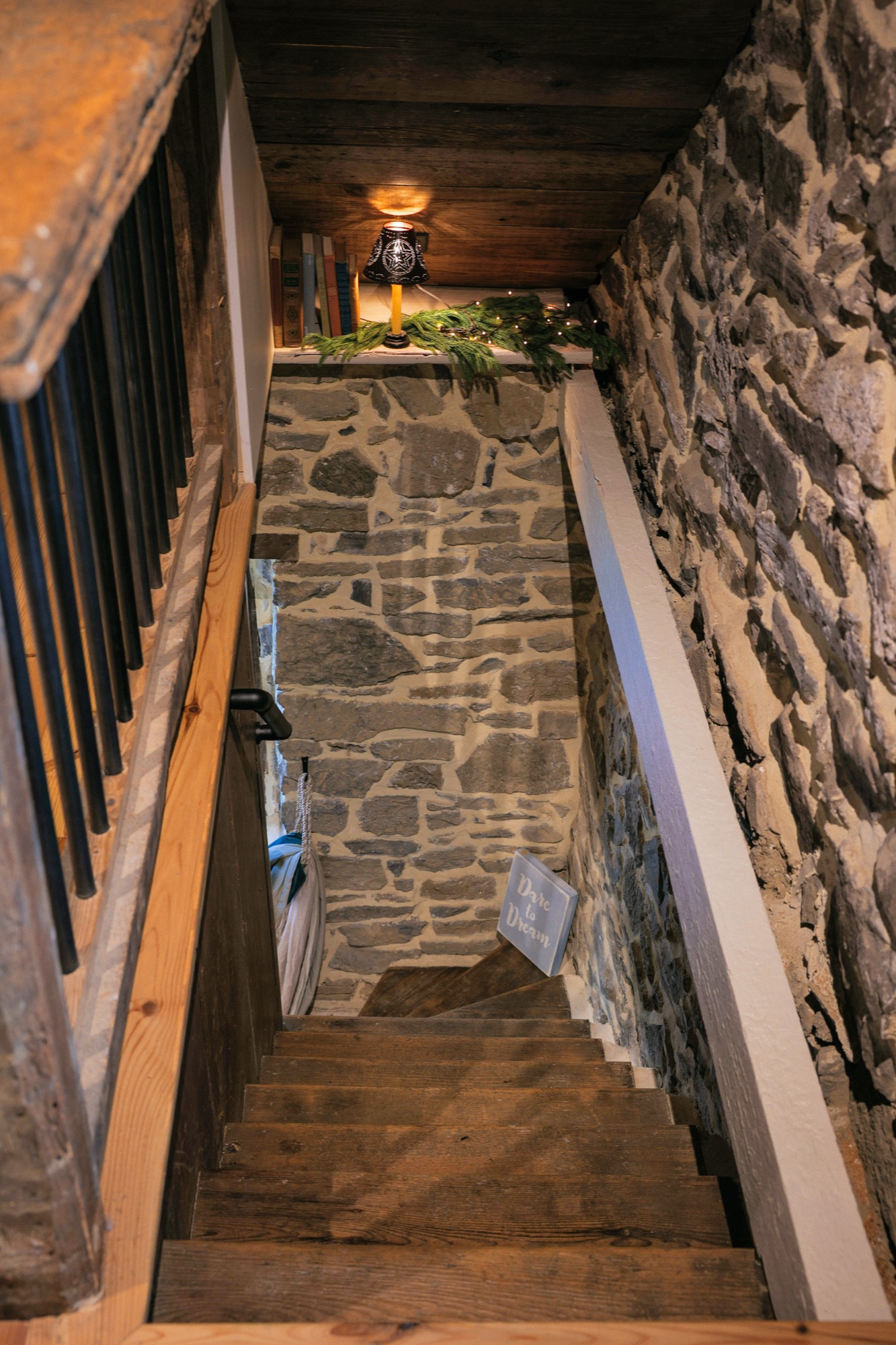 Looking down a narrow enclosed stair, fieldstone along the far and right-hand walls, a hewn post at the left