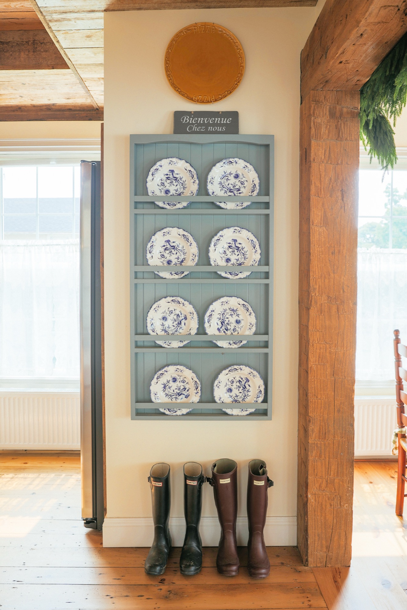 A blue-grey plate rack of blue-and-white transferware beneath a small board reading Bienvenue Chez nous.